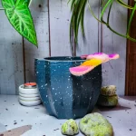 Maceta Zucca Azul Marino de concreto con forma de calabaza y 12 puntas, acabado jaspeado, en ambiente interior moderno con planta.