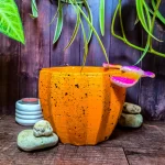 Maceta Zucca Naranja de concreto con forma de calabaza y 12 puntas, acabado jaspeado, en ambiente interior moderno con planta.